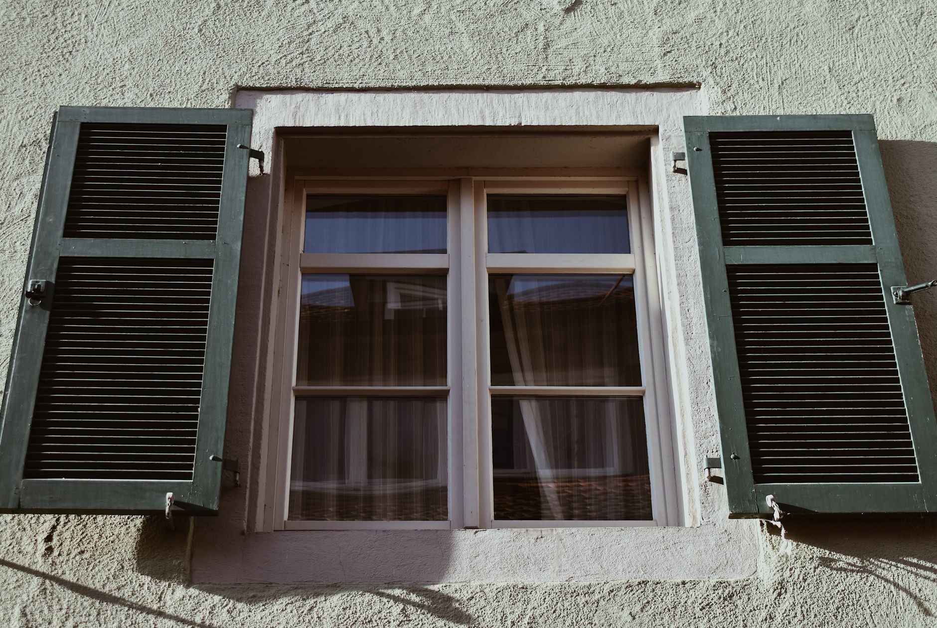 Close-up of a classic window with open green shutters on an aged stucco wall in Riverside, CA